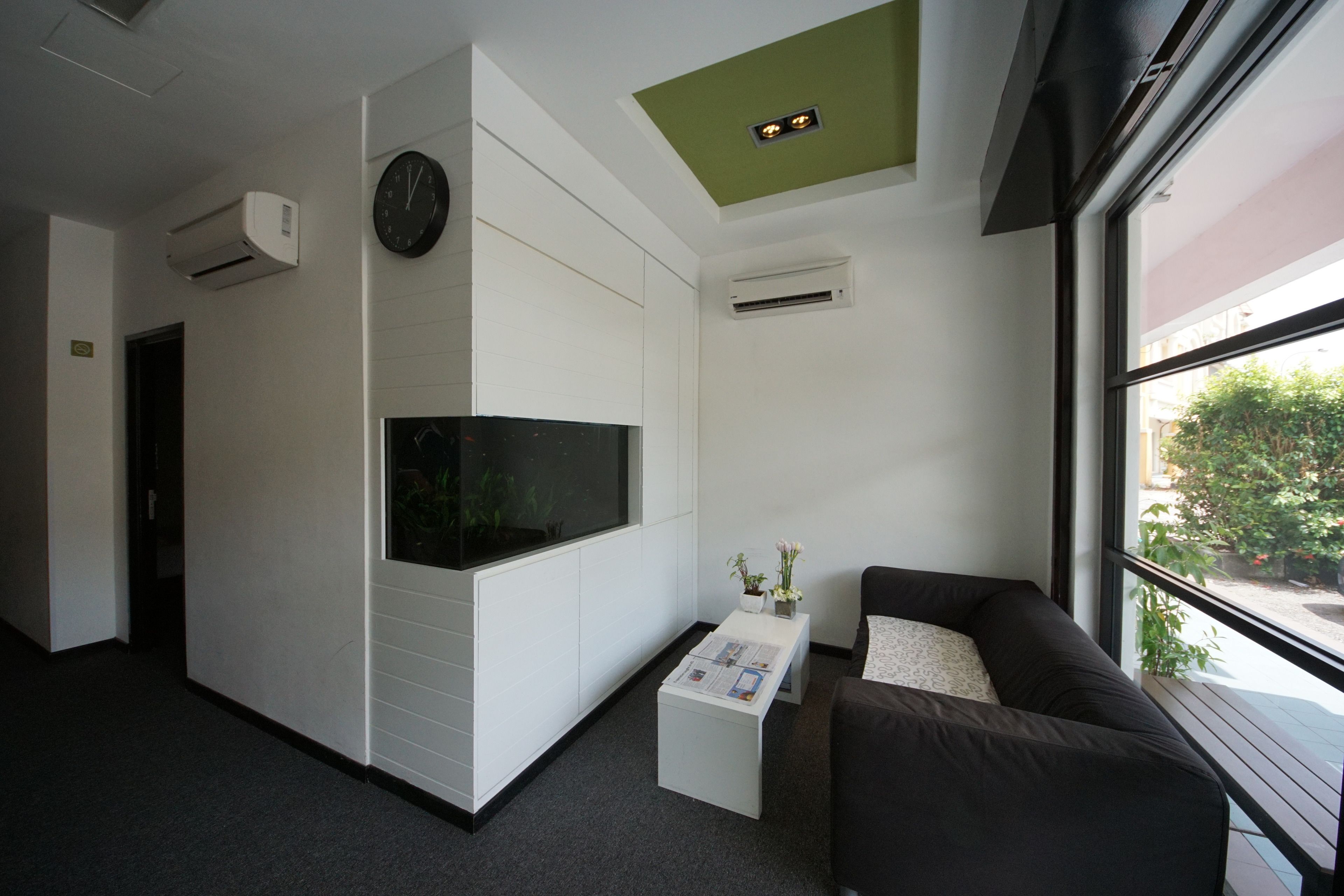 Un espacio de oficina moderno con un ventanal grande, un sofá negro, una mesa de centro blanca y un reloj en la pared.
