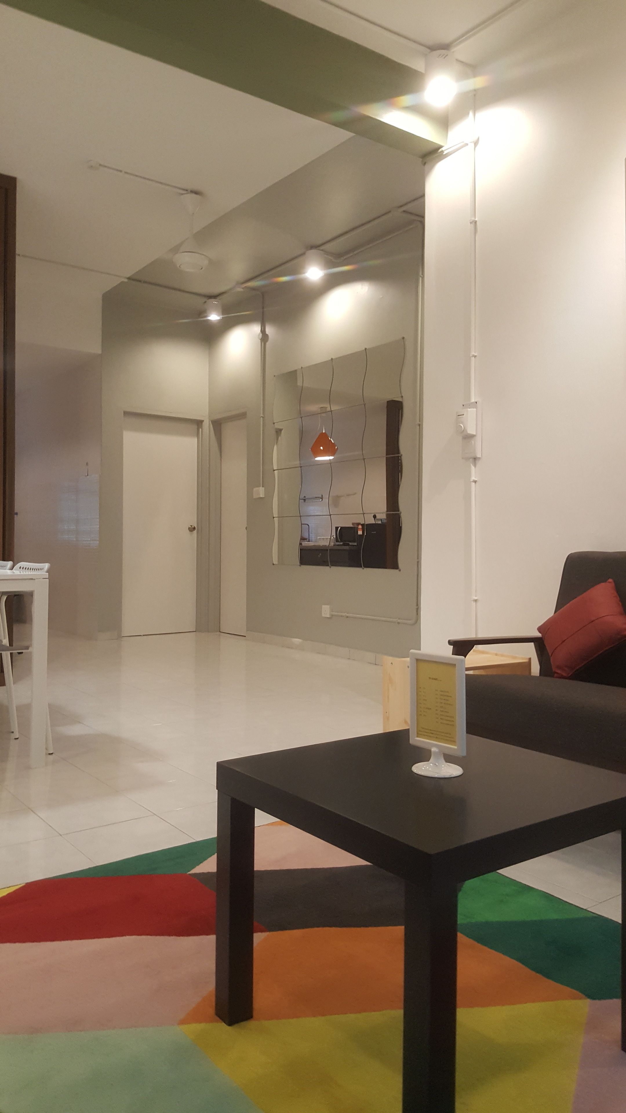 Een modern interieur met een zwarte tafel, een kleurrijk vloerkleed, een bank met een rode kussen en een spiegel aan de muur.