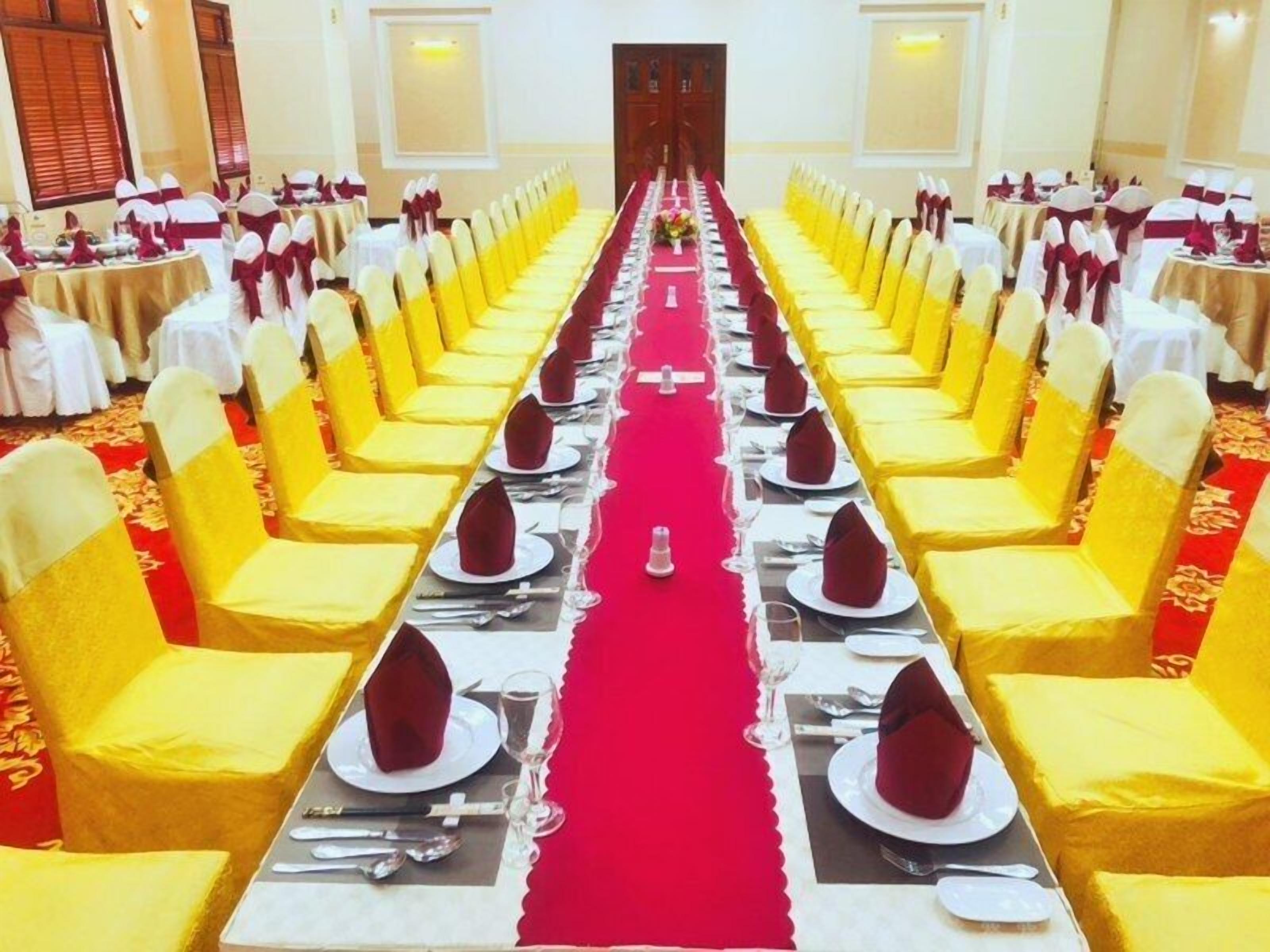 A banquet hall with rows of tables set for a formal event, featuring yellow chairs and red table runners.