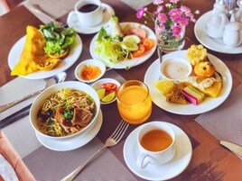 Una mesa dispuesta con varios platos, incluyendo un tazón de fideos, una fuente de frituras, un vaso de zumo de naranja y una taza de té.
