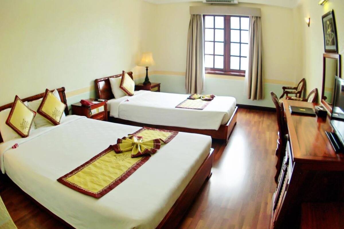 Habitación de hotel con dos camas, un escritorio, una silla, un televisor y una ventana con cortinas.