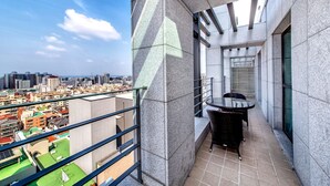 A narrow balcony with a view of a cityscape, a small table with chairs, and a glass railing. - Jeju Central City Hotel (Jeju-si,)