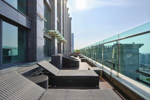 A rooftop terrace with outdoor seating and a glass railing overlooking a cityscape. - Jeju Central City Hotel (Jeju-si,)