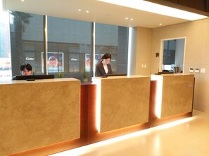 A reception area with three counters, a large window with reflections, and a Cartier store in the background. - Jeju Central City Hotel (Jeju-si,)