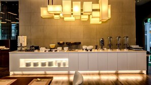 A modern reception desk with a geometric light fixture above, a counter with various amenities, and a clean, minimalist design. - Jeju Central City Hotel (Jeju-si,)