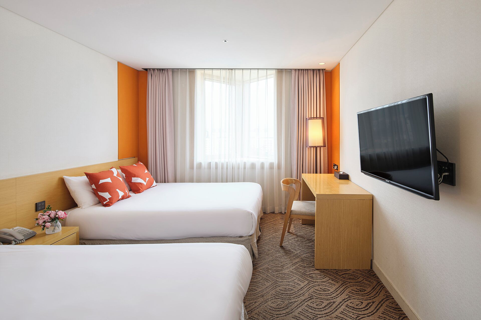 A hotel room with two beds, a desk, a TV, and a window with curtains.