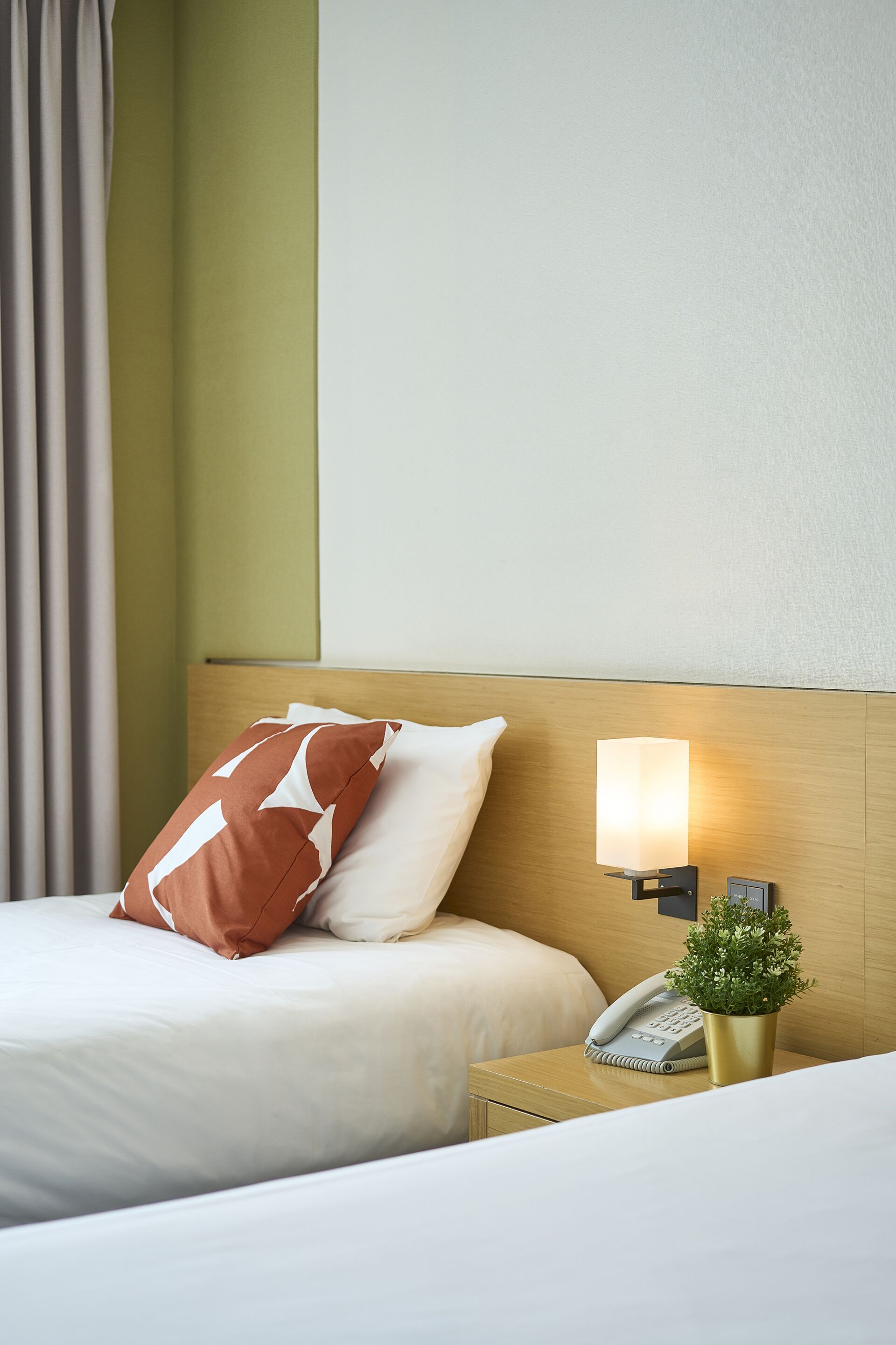 Une chambre d’hôtel avec un lit, une table de chevet avec une lampe, un téléphone et une petite plante.