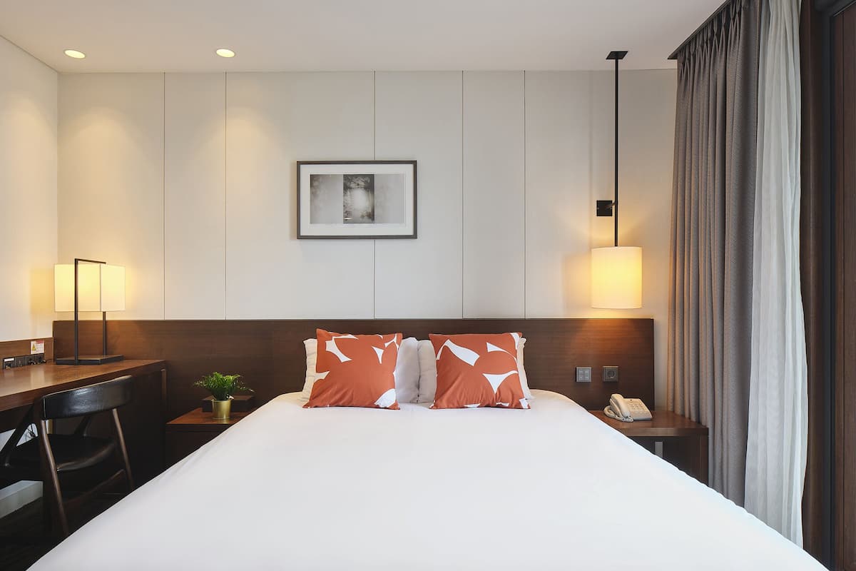 Une chambre d’hôtel avec un grand lit, un bureau avec une lampe, un téléphone et un tableau encadré au mur.
