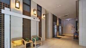 Un hall d’hôtel comprenant des espaces d’attente, un comptoir d’accueil et un ascenseur.