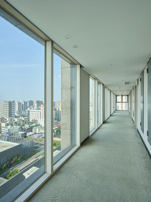 A long, narrow corridor with large windows on one side, leading to a door at the end. - Jeju Central City Hotel (Jeju City)