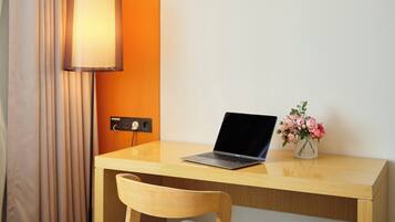 Une chambre d’hôtel avec un bureau en bois, un ordinateur portable, un vase avec des fleurs et une lampe.