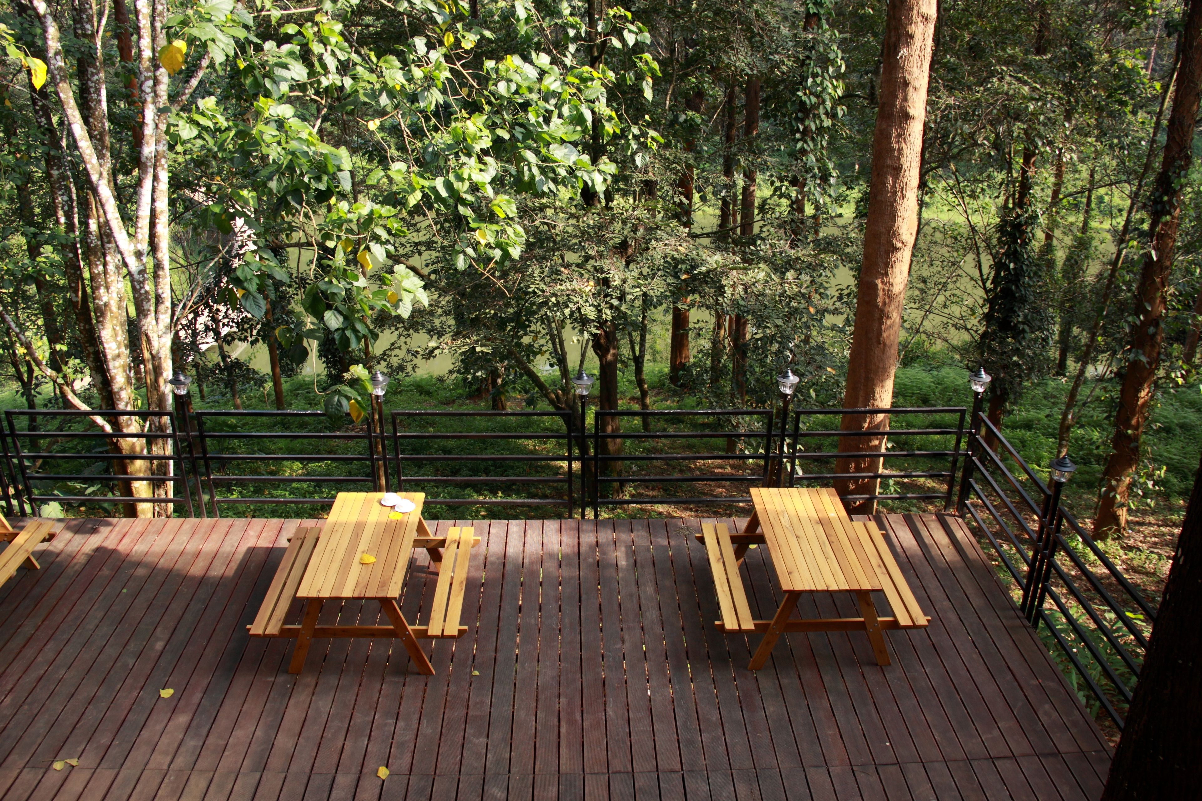 A wooden deck with picnic tables and a railing overlooking a forested area.