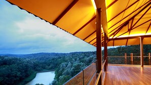 Um deck de madeira com guarda-corpo de vidro, com vista para um rio e paisagem arborizada.