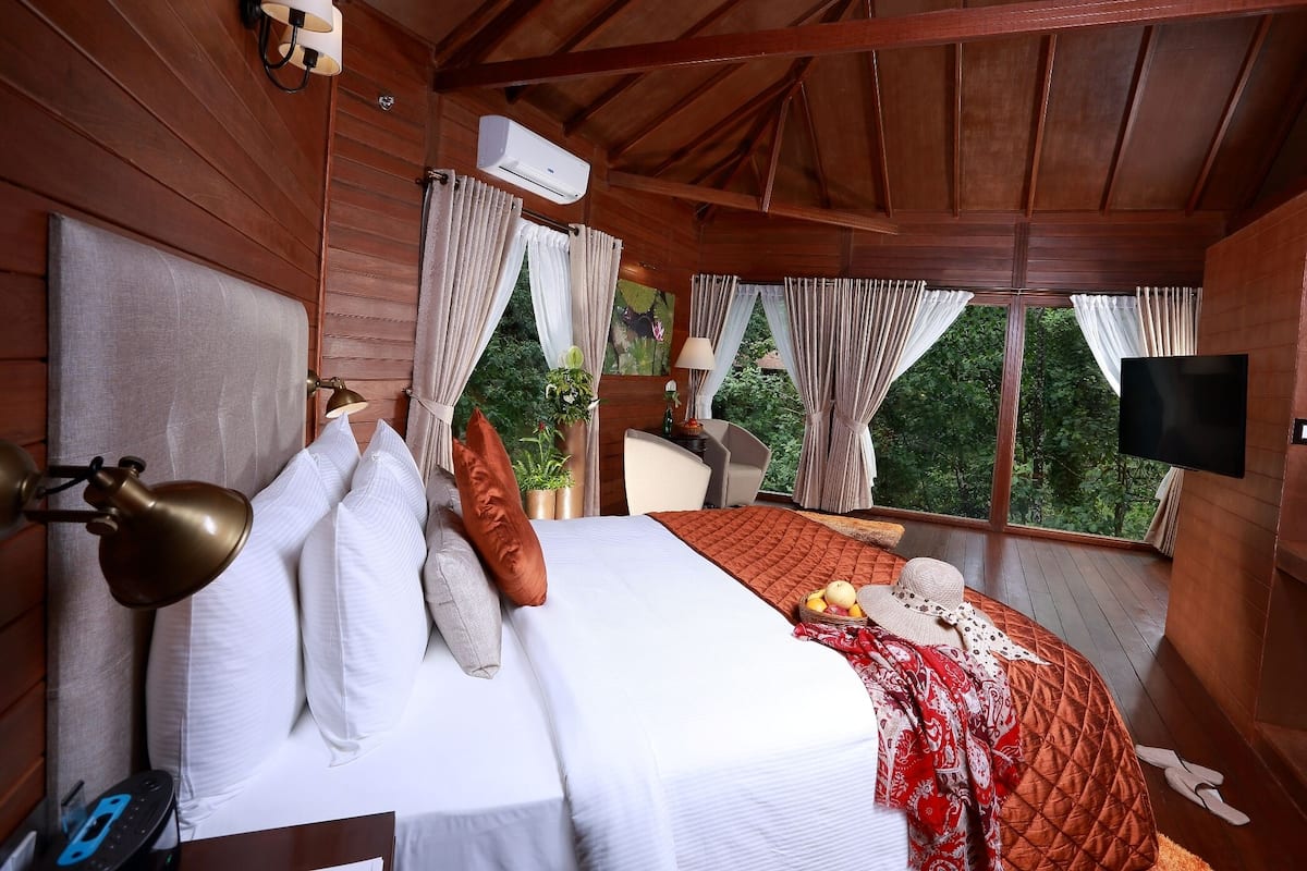 A wooden cabin bedroom with a bed, bedside lamps, a TV, and a window with curtains.