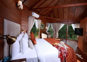A wooden cabin bedroom with a bed, bedside lamps, a TV, and a window with curtains.