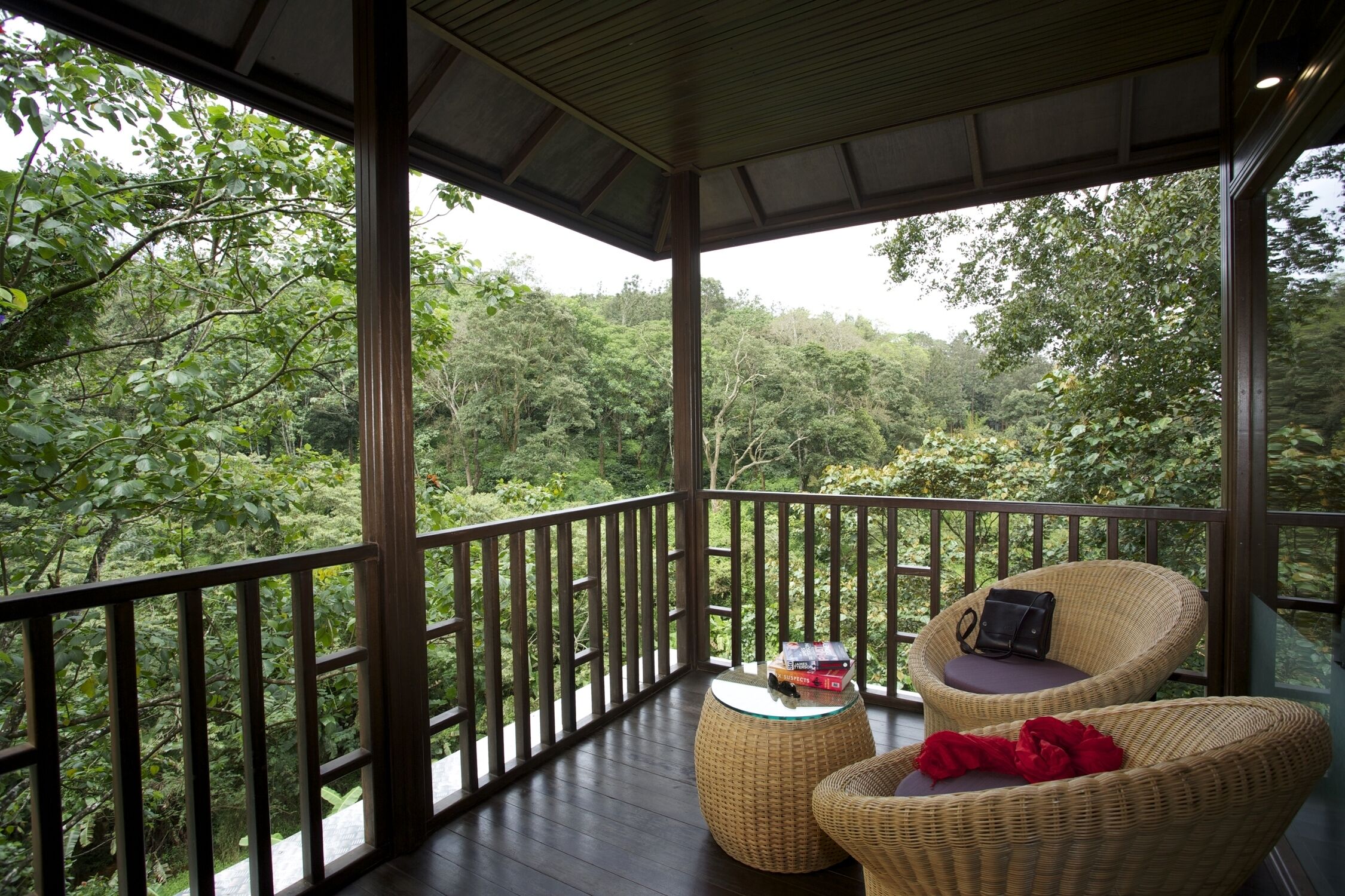 Ein Balkon mit Korbmöbeln, einem kleinen Tisch und Blick auf einen dichten Wald.