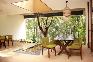 A dining area with a table set for four, surrounded by chairs, and a view of a forest through large windows.