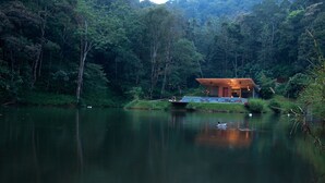 Um cenário tranquilo à beira de um lago, com uma construção de madeira, rodeada por uma floresta densa.