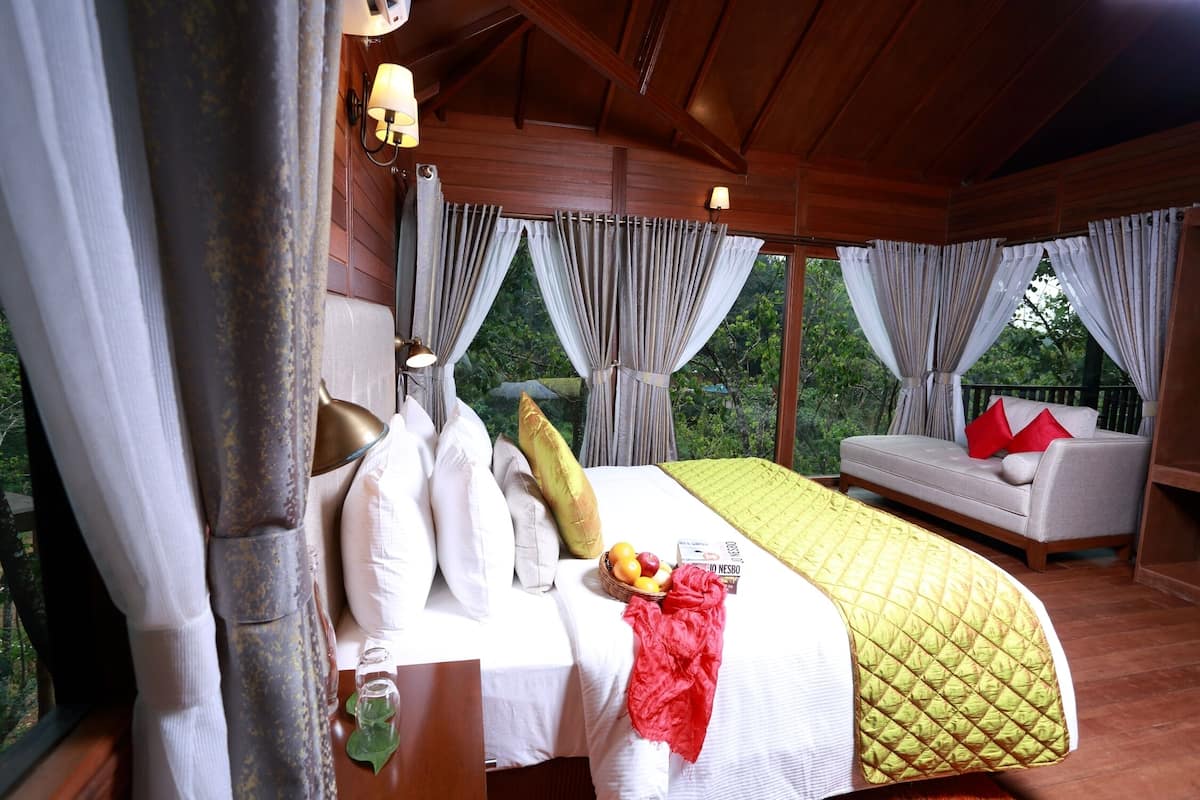 A wooden cabin bedroom with a bed, pillows, a basket of fruit, and a sofa with red cushions.
