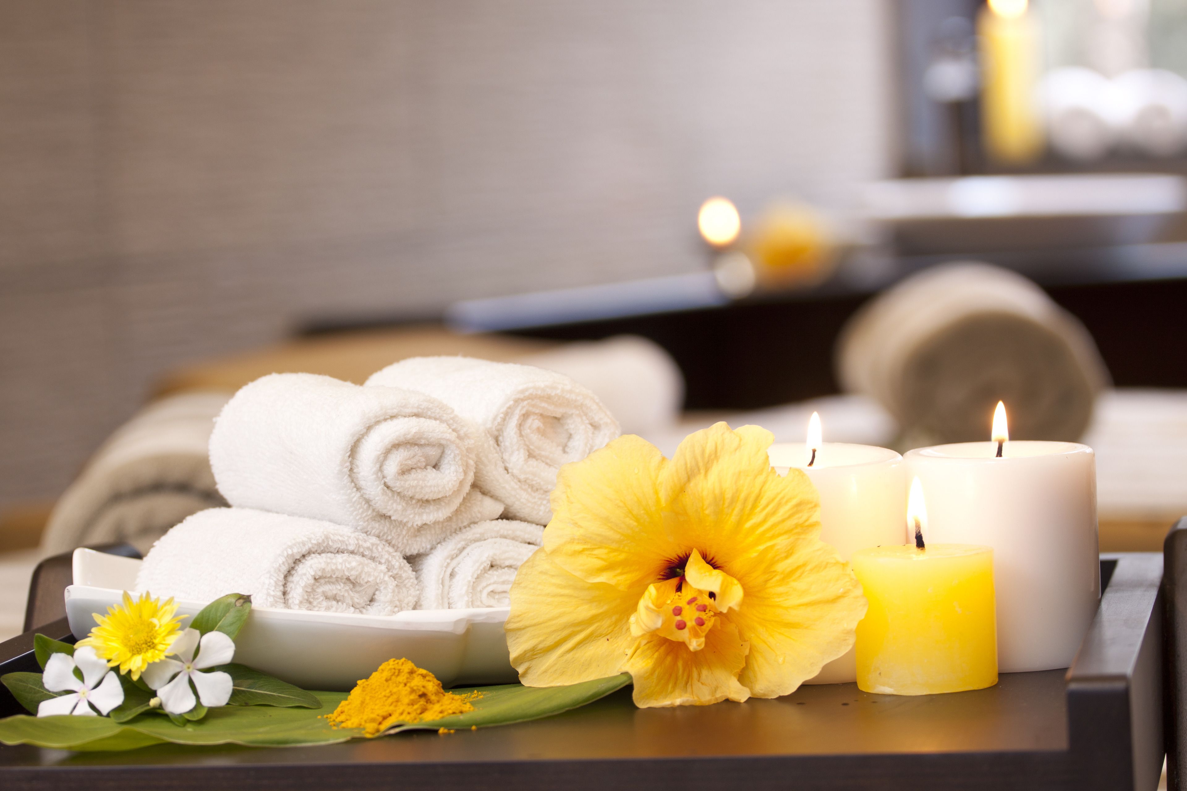 A spa setting with towels, candles, and flowers on a tray.