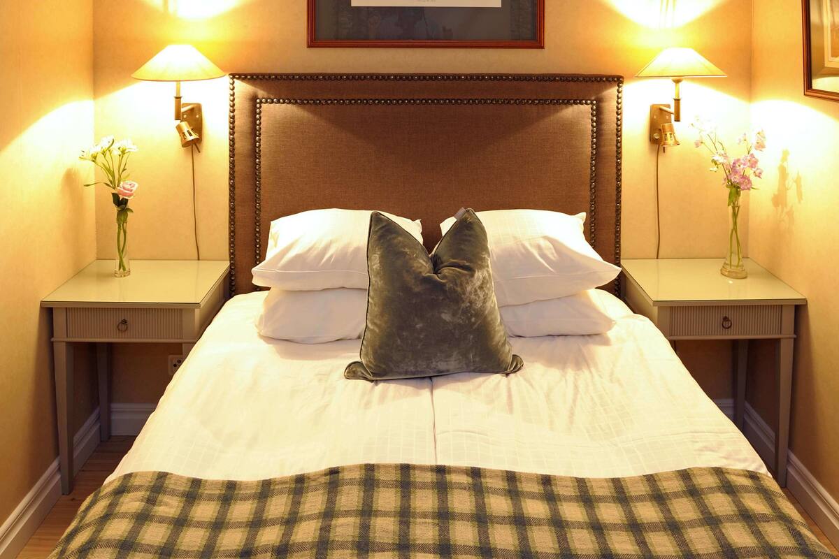 A neatly made bed with a plaid throw blanket, two bedside tables with lamps, and a framed picture on the wall.