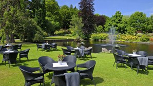 An outdoor seating area with wicker tables and chairs, a pond, and a fountain. - Thorskogs Slott (Västerlanda)
