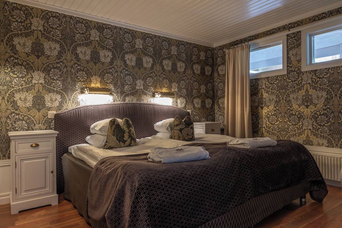A bedroom with a large bed, two bedside tables, a nightstand, and a window with curtains.