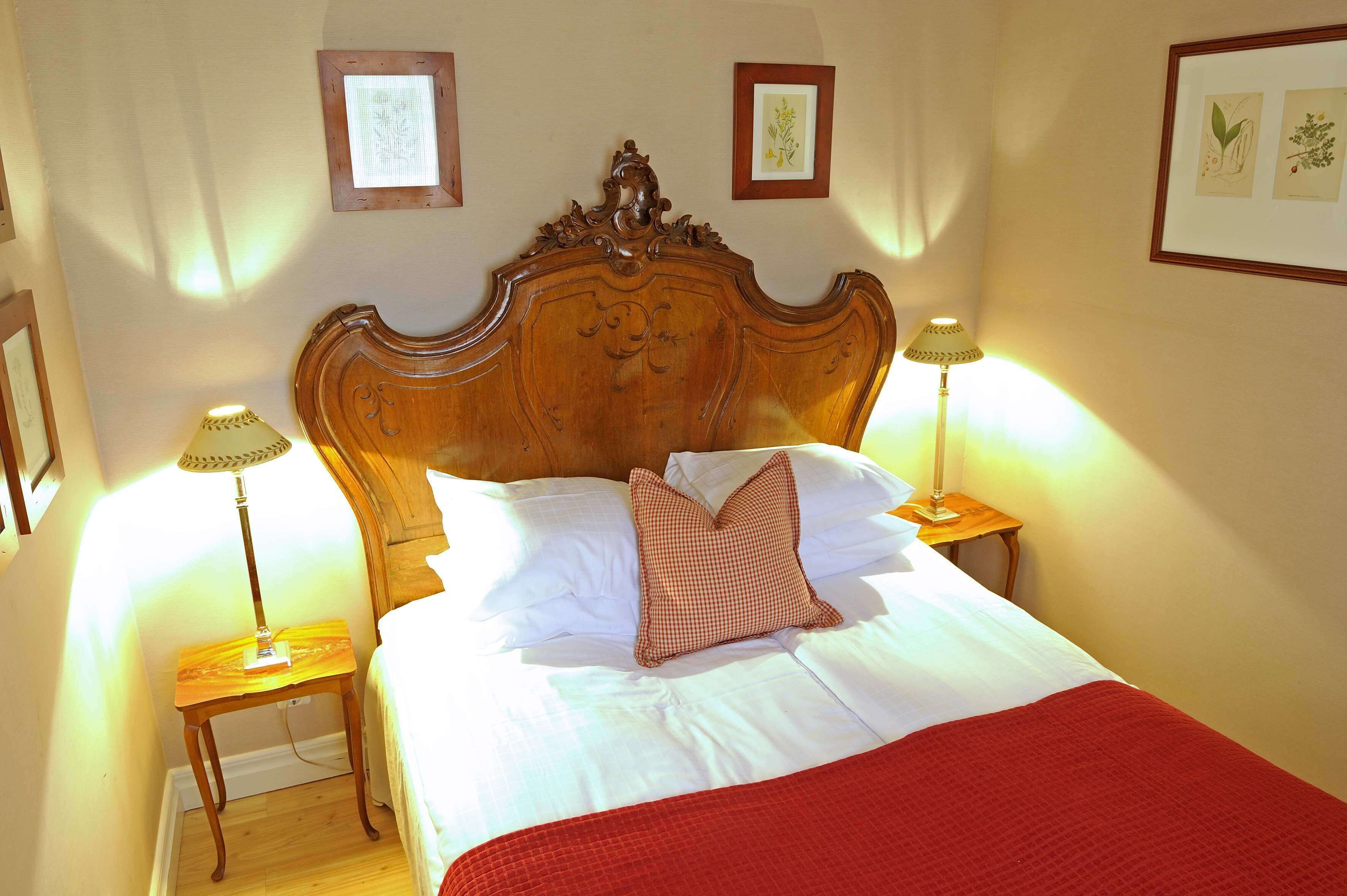 A neatly made bed with a wooden headboard, two bedside lamps, and a red throw blanket.