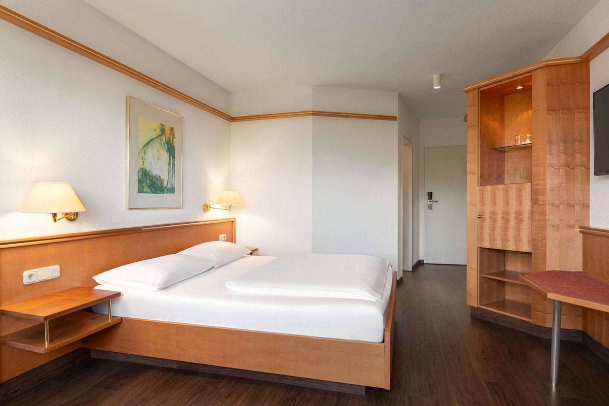 Ein Hotelzimmer mit Bett, Nachttischlampen, einem Bild an der Wand und einem Holzschrank mit Fernseher.