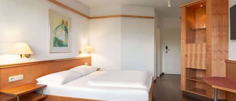 A hotel room with a bed, bedside lamps, a painting on the wall, and a wooden cabinet with a TV.