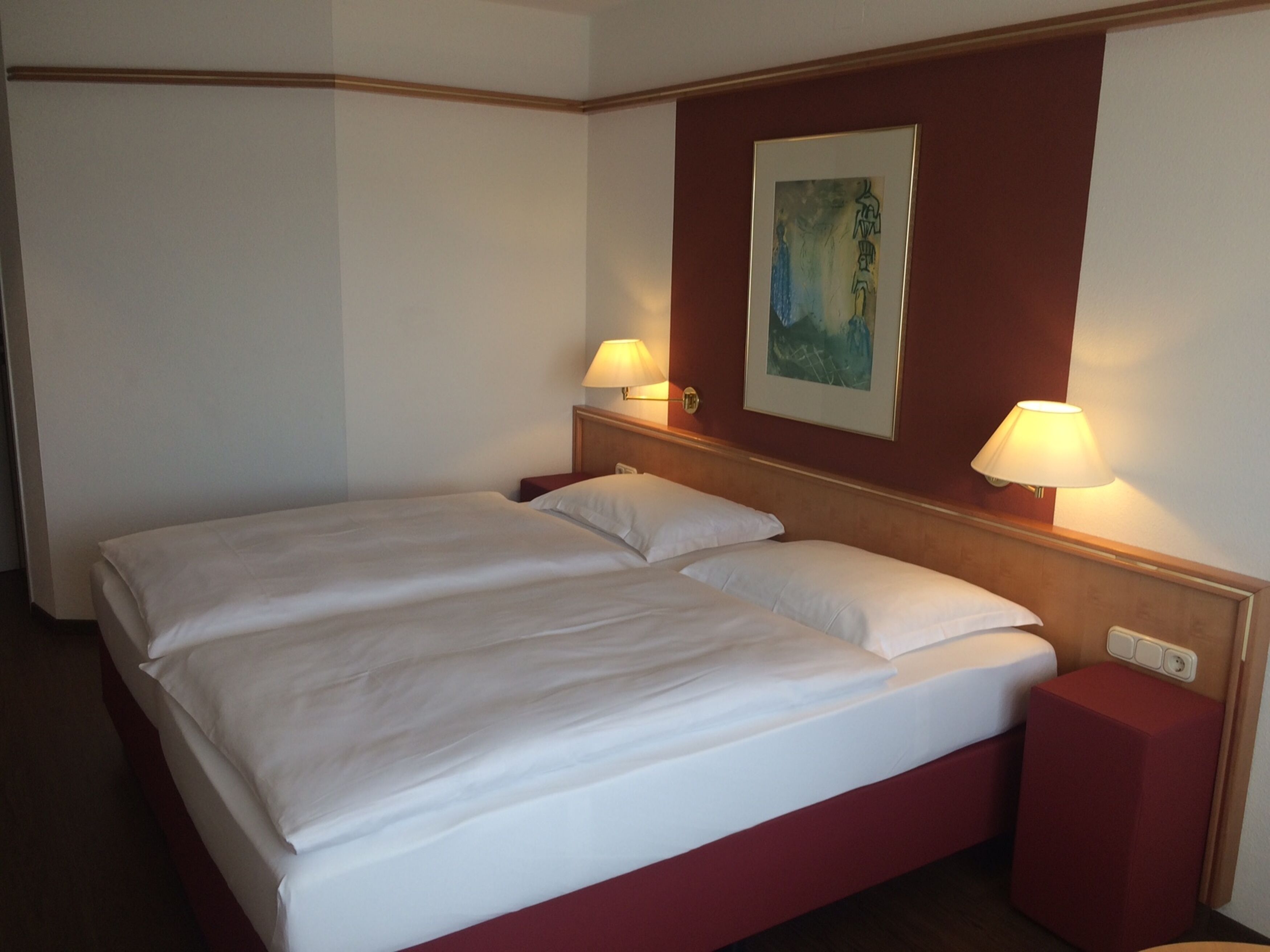 Un lit double avec du linge de lit blanc, deux tables de chevet avec des lampes et un tableau au mur.