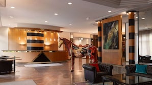 A modern lobby with a reception desk, leather seating, a colorful abstract painting, and a large horse sculpture. - Amedia Weiden, Trademark Collection by Wyndham (Weiden in der Oberpfalz)