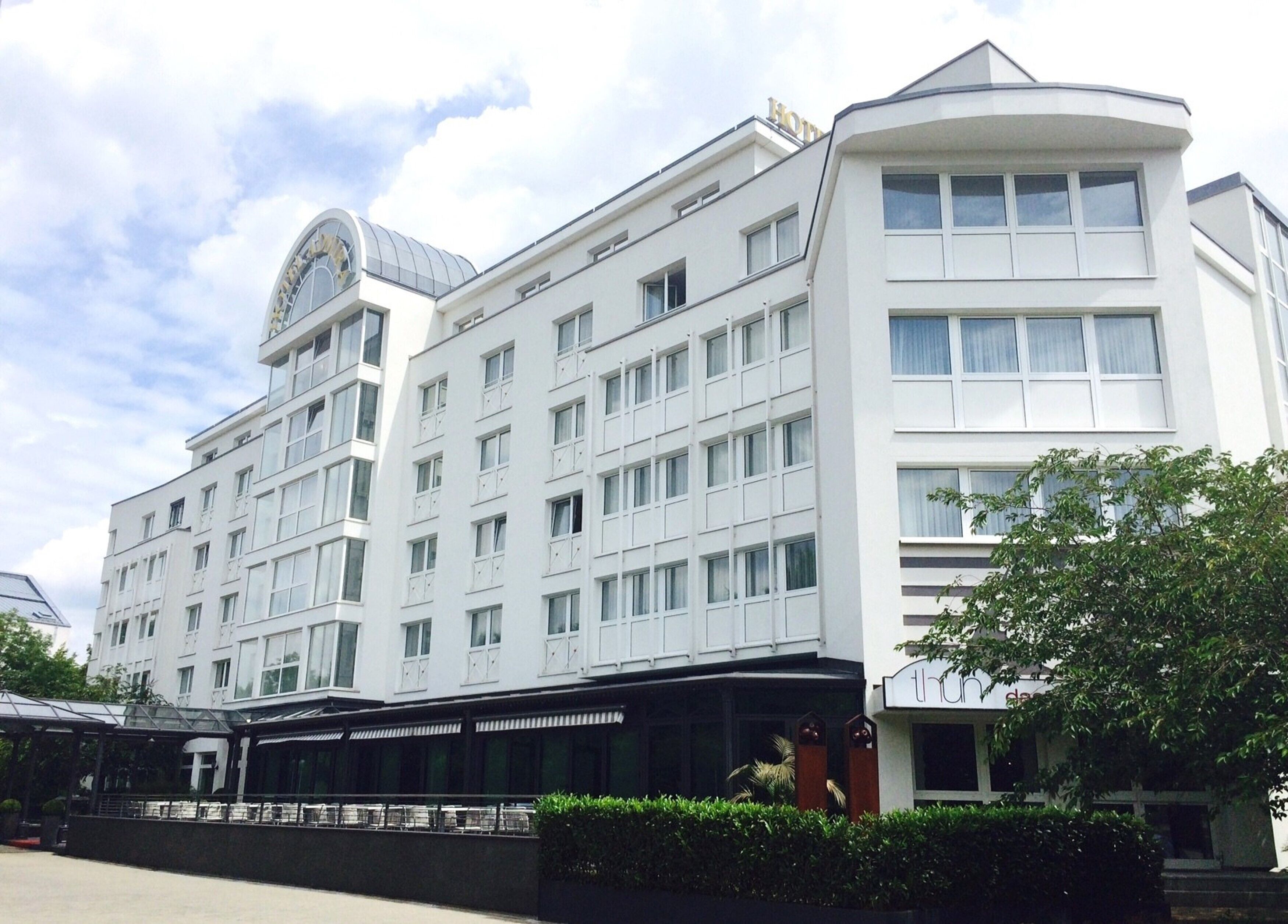 A modern hotel with a symmetrical facade, multiple windows, and a distinctive dome structure on the left.