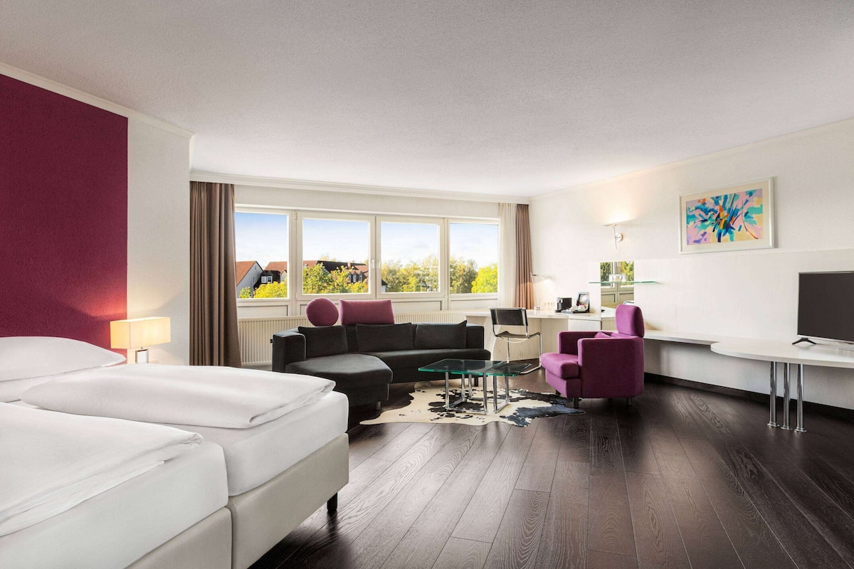 Ein Hotelzimmer mit Bett, Sofa, Schreibtisch und Fernseher.