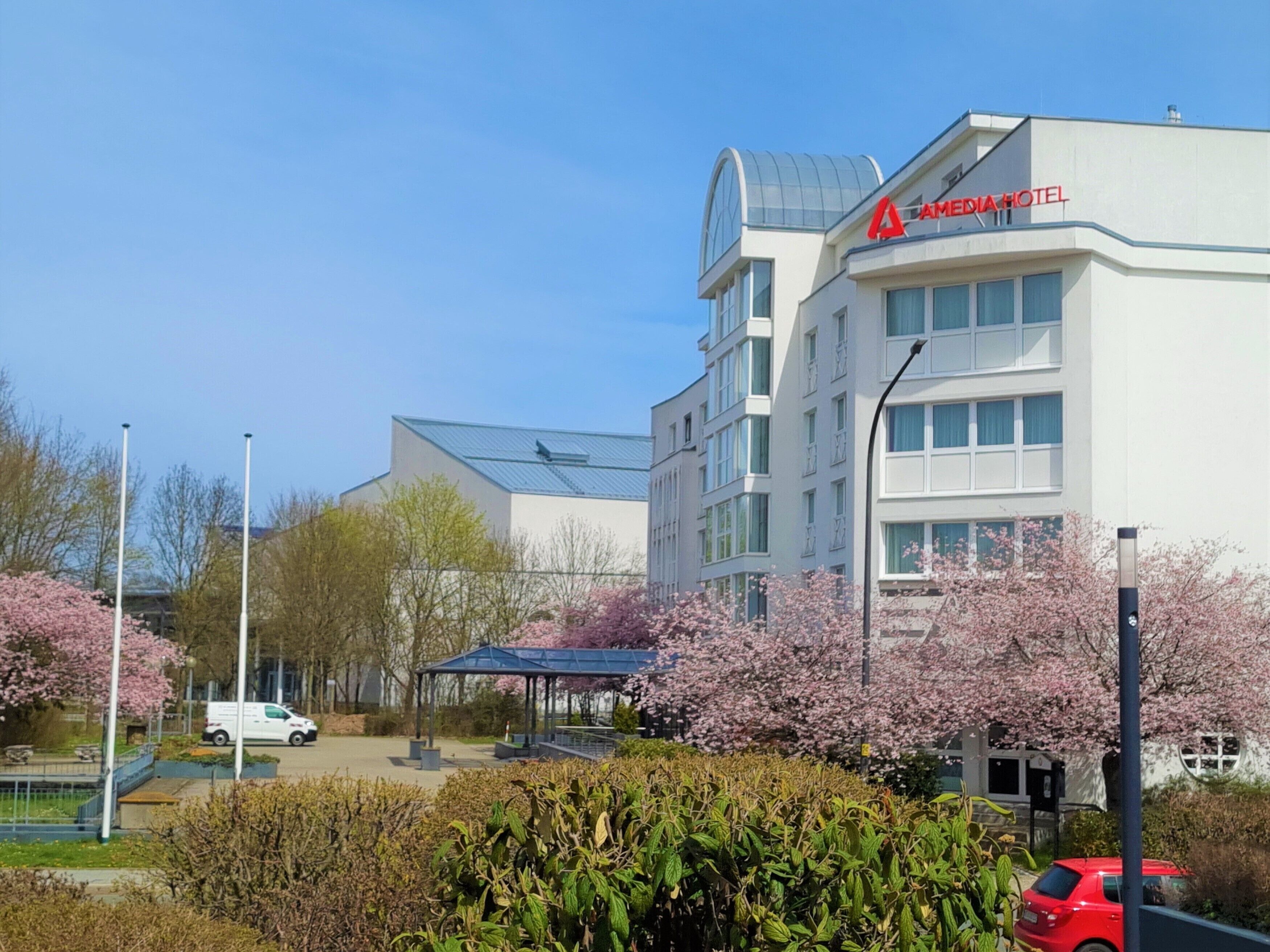 A modern hotel with a prominent "AMEDIA HOTEL" sign, featuring a contemporary design with large windows and a covered outdoor area.