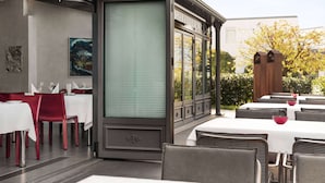 An outdoor dining area with tables and chairs, a large window, and a view of the surrounding area. - Amedia Weiden, Trademark Collection by Wyndham (Weiden in der Oberpfalz)