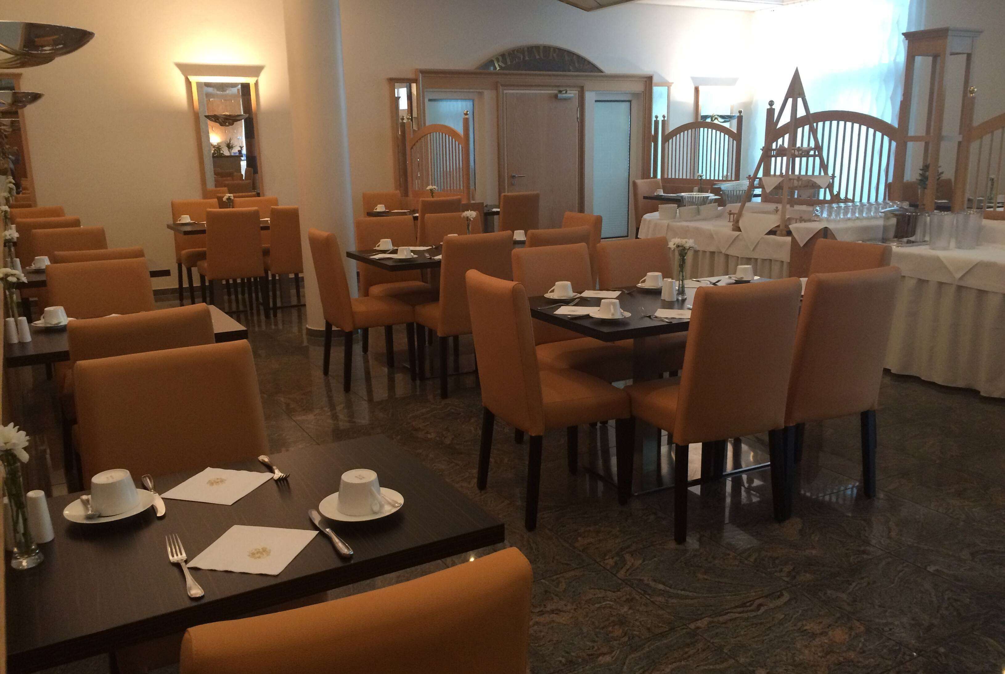 Comedor con mesas dispuestas para cuatro comensales, cada una con sillas color naranja, manteles blancos y cubiertos y servilletas ordenados.