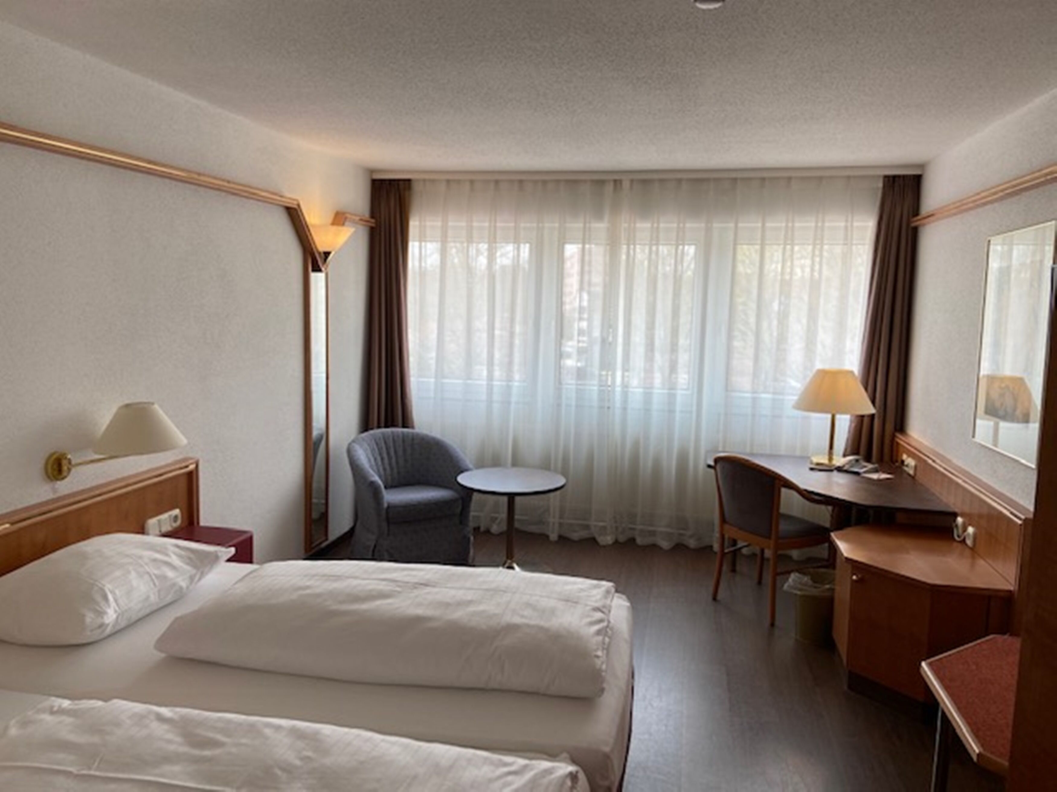 Una camera d'albergo con un letto, una scrivania, una sedia, un tavolino e una lampada.