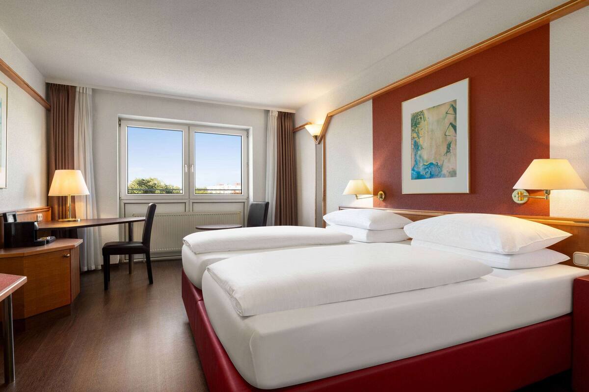 Ein Hotelzimmer mit zwei Betten, einem Schreibtisch, einem Stuhl und einem Fenster mit Vorhängen.