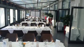 A restaurant with multiple tables set for dining, featuring a modern interior with glass partitions and potted plants.