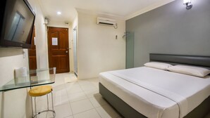A bedroom with a bed, a glass table with a stool, a TV mounted on the wall, and an air conditioning unit. - Dju Dju Hotel (Batam)