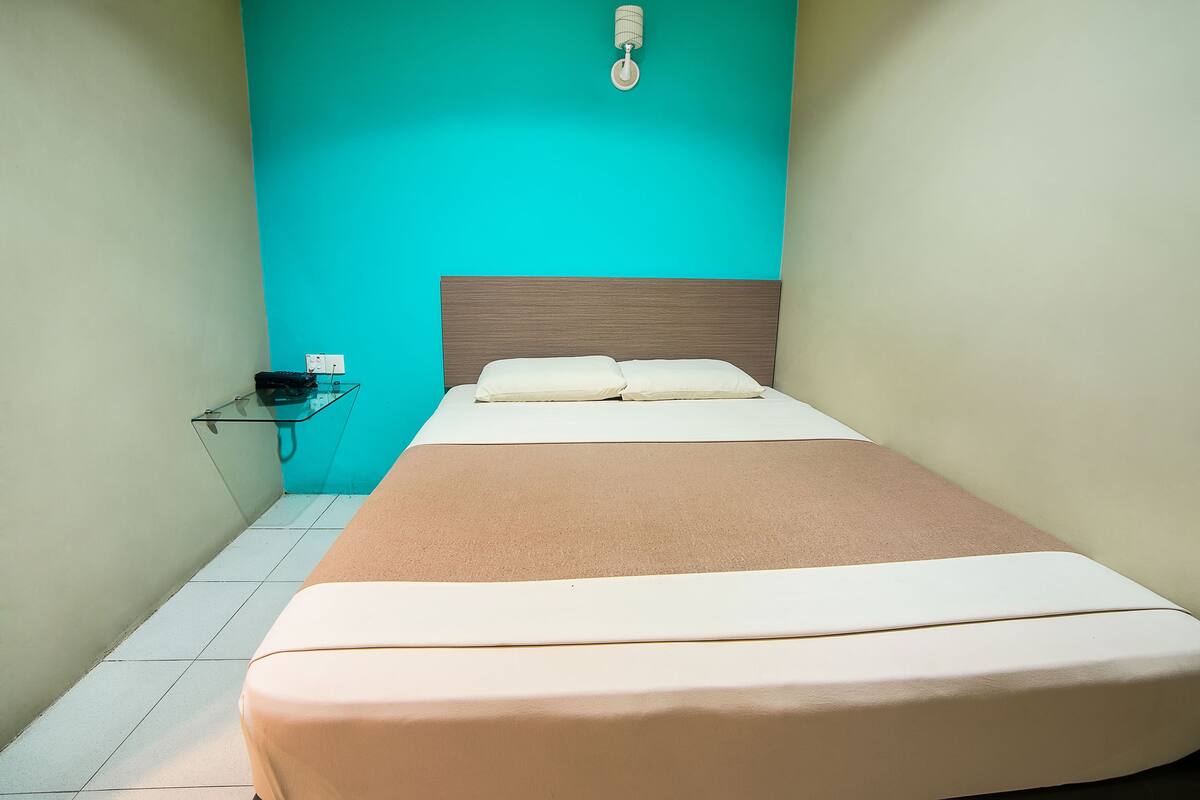 A bed with a wooden headboard, a glass side table, and a wall-mounted light fixture.