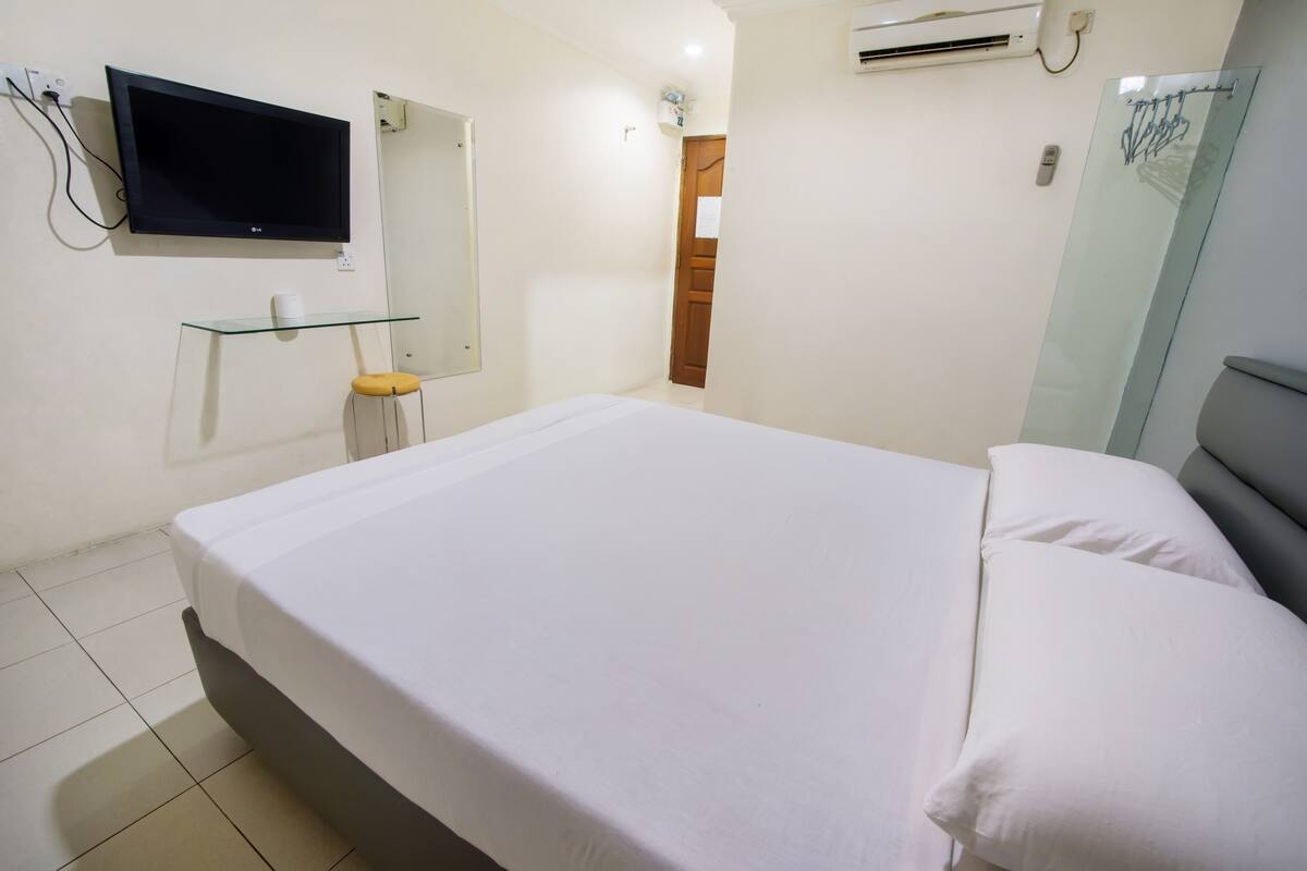 A bedroom with a bed, a TV mounted on the wall, a glass shelf, and an air conditioning unit.