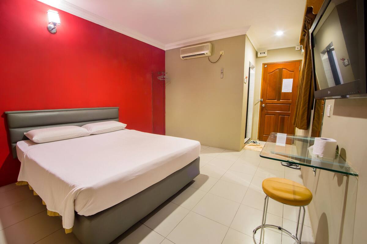 A hotel room with a bed, a glass table with a stool, a TV, and a door.
