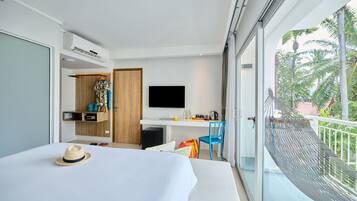 A modern hotel room with a bed, a TV, a desk with a chair, and a balcony with a view of palm trees.