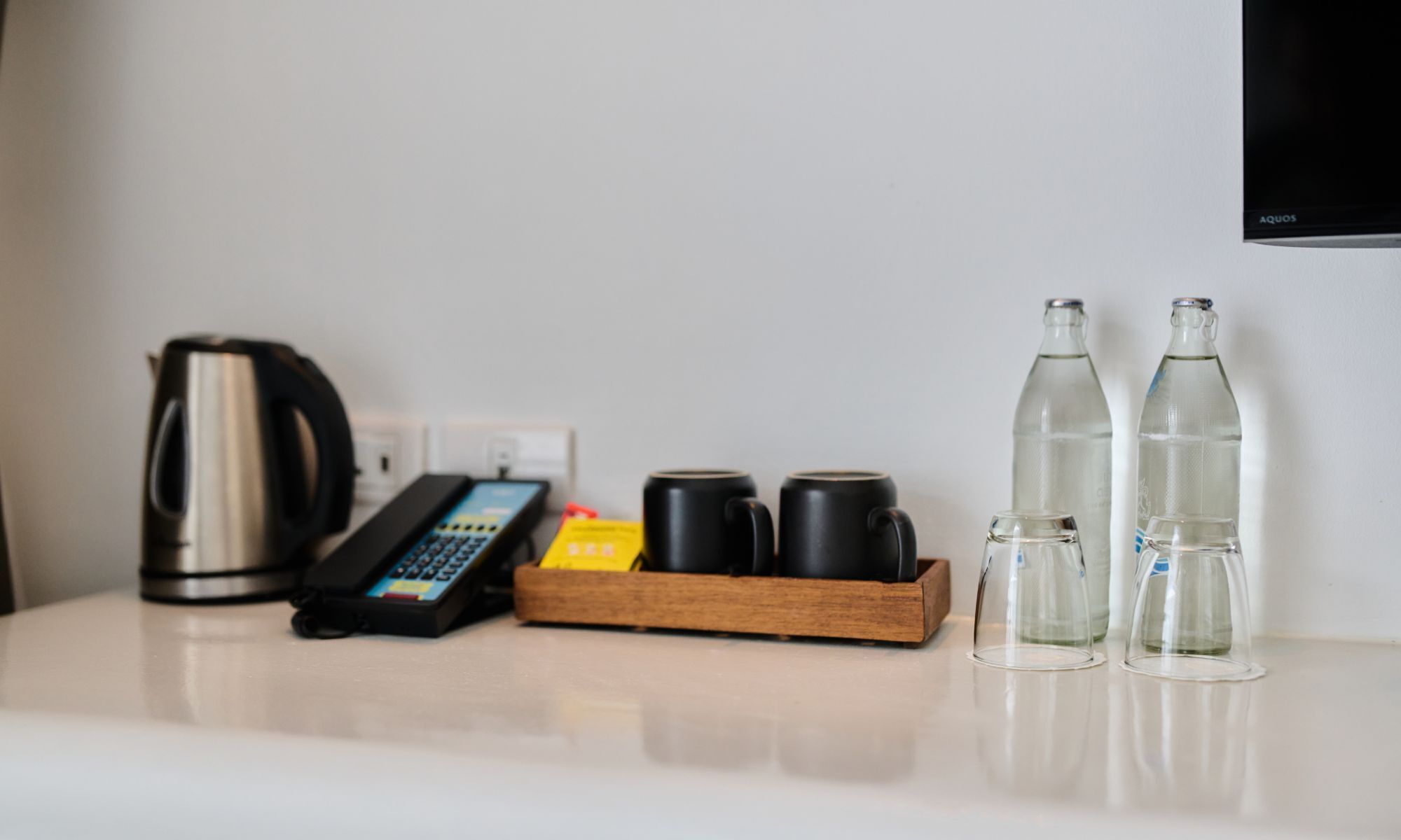 Une chambre d’hôtel équipée d’une machine à café, d’un téléphone, d’un plateau avec des tasses et de deux bouteilles d’eau.