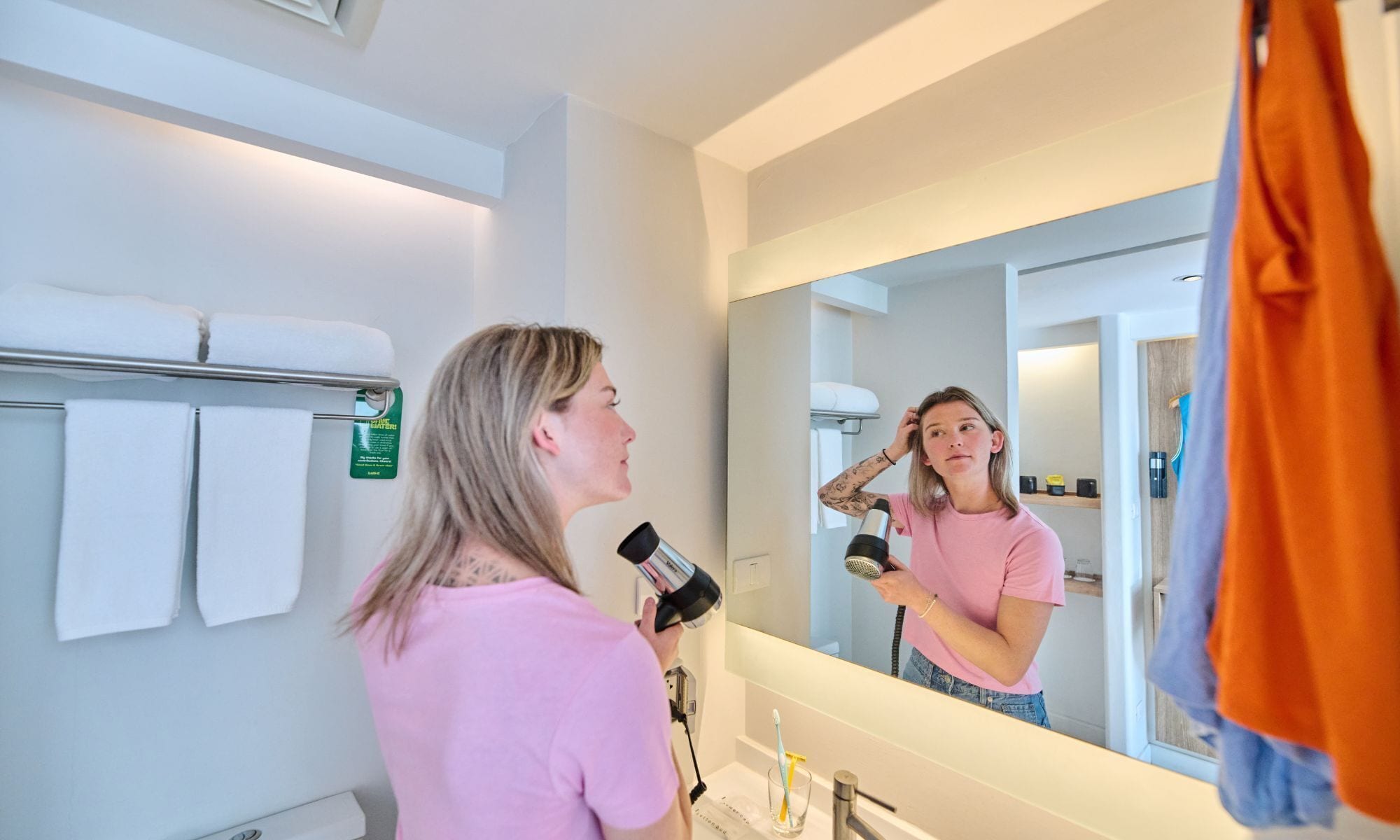 A bathroom with a large mirror, a towel rack with white towels, and a glass of water on the counter.