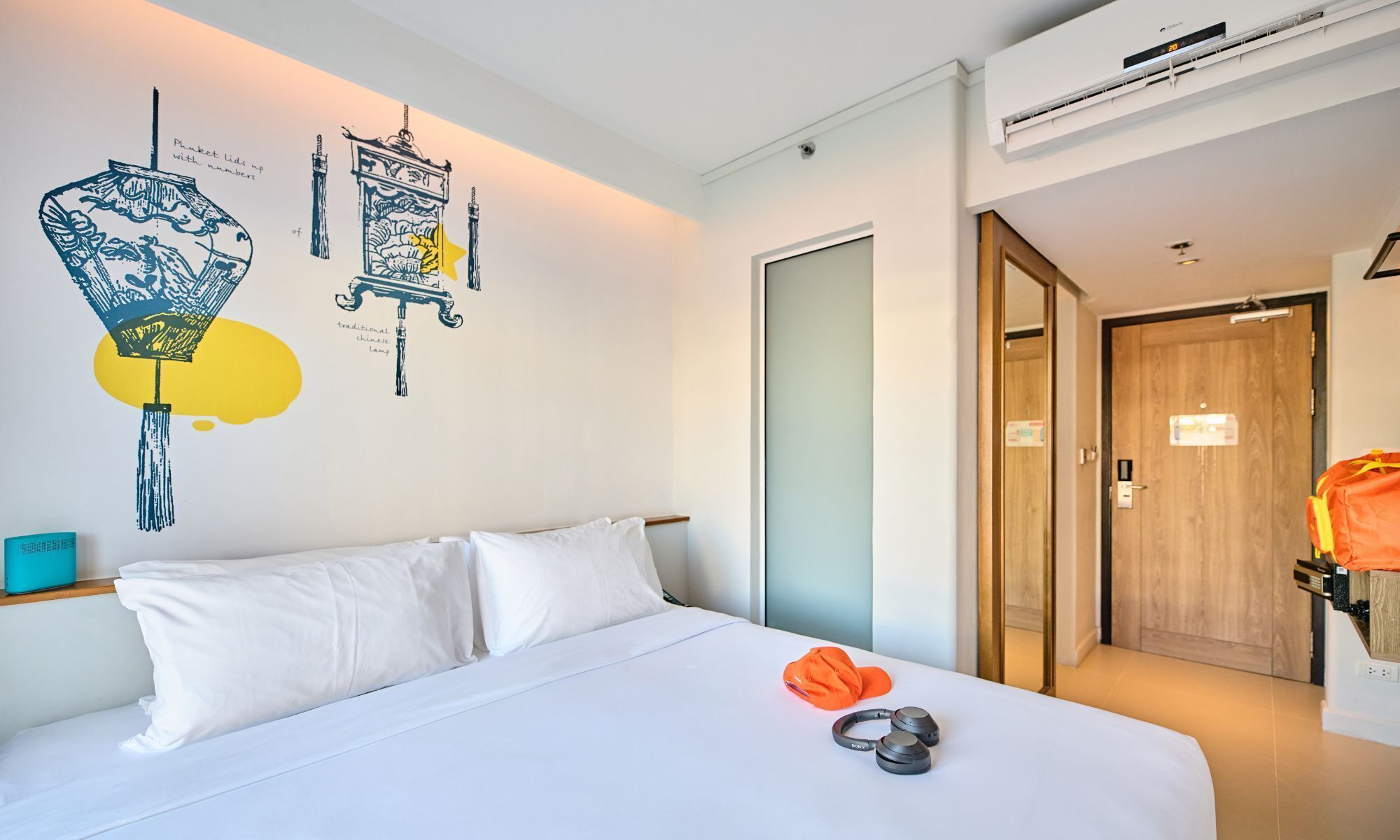 A hotel room with a bed, white bedding, a wall with traditional Chinese lamp illustrations, and a door leading to another room.