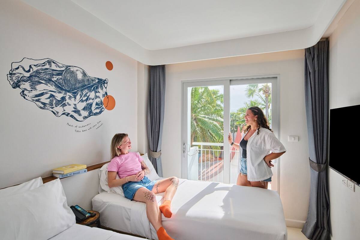 A hotel room with a bed, a TV, a window with curtains, and a wall with a decorative piece.