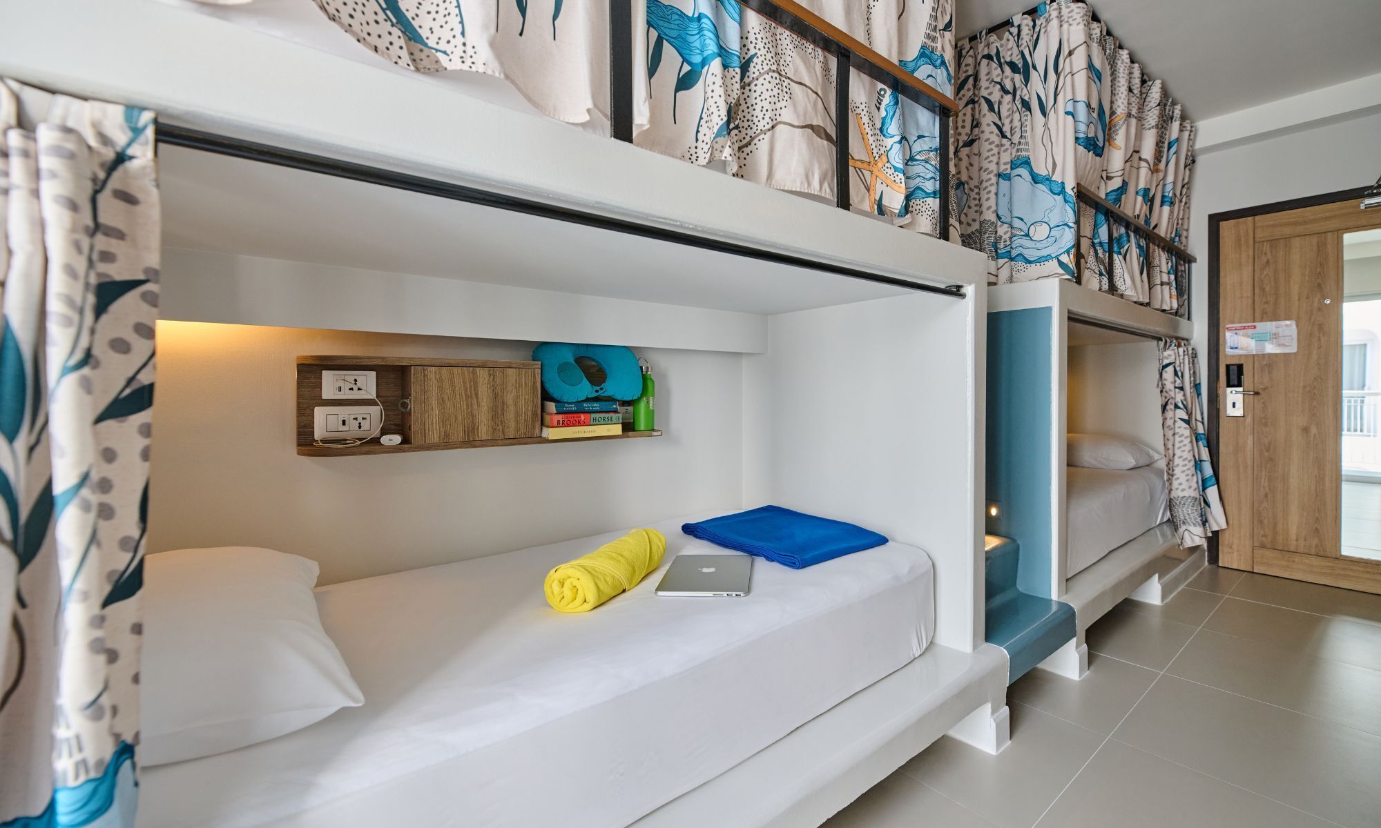 A bunk bed room with a shelf above the lower bunk holding books and a power outlet.